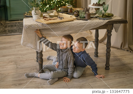 Funny naughty boys are sitting under the Christmas table, waiting for a holiday and miracles Funny naughty boys are sitting under the Christmas table, waiting for a holiday and miracles 131647775
