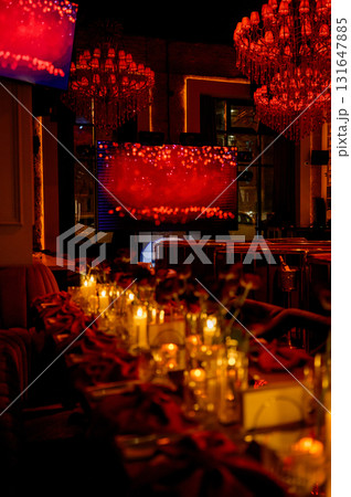 Close-up of a long table with flowers and burning candles in a dark room 131647885