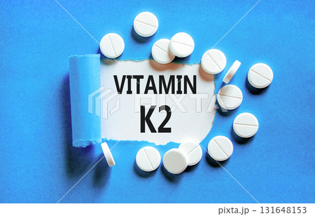 Vitamin K2 phylloquinone symbol. Concept words Vitamin K2 on beautiful white paper. White pills tablets. Beautiful blue background. Medical healthy lifestyle Vitamin K2 phylloquinone concept. 131648153