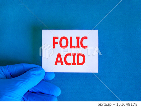 Folic acid symbol. Concept words Folic acid on beautiful white card. Doctor's hand in blue medical glove. Beautiful blue background. Medical healthy lifestyle folic acid concept. Folic acid symbol. Concept words Folic acid on beautiful white card. Doctor's hand in blue medical glove. Beautiful blue background. Medical healthy lifestyle folic acid concept. 131648178