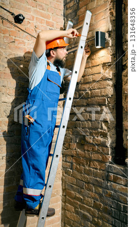 Engineer using ladder to repair lighting system on brick wall Engineer using ladder to repair lighting system on brick wall 131648356