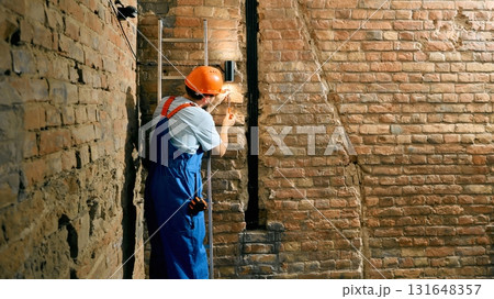 Technician repairing wall light fixture in brick corridor Technician repairing wall light fixture in brick corridor 131648357
