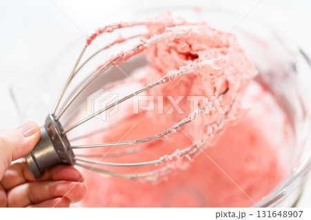 A hand holds a whisk full of raspberry buttercream frosting, freshly whipped for Easter Cookie Sandwich with Raspberry Buttercream. 131648907