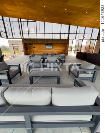A bright lounge space with outdoor seating and tall windows inside a community clubhouse. The room features a wood-paneled ceiling and minimalist furnishings. A bright lounge space with outdoor seating and tall windows inside a community clubhouse. The room features a wood-paneled ceiling and minimalist furnishings. 131648922