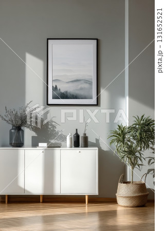 Modern interior with a framed artwork on a gray wall above a white cabinet, decorated with vases, plants, and natural sunlight Modern interior with a framed artwork on a gray wall above a white cabinet, decorated with vases, plants, and natural sunlight 131652521