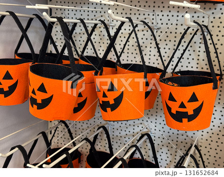 Orange felt buckets with jack o lantern faces and black handles on retail display. Halloween container, candy collection, seasonal festivity, tradition, playful celebration and autumn folklore. 131652684