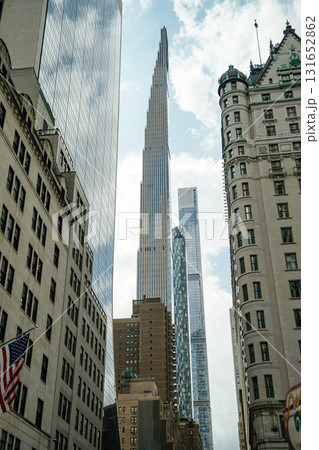 A sleek, ultra-tall skyscraper rises sharply above older, historic buildings in New York City's Midtown area. The contrast between classic architecture and contemporary glass towers creates a dramatic 131652862