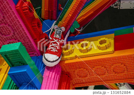 A small mouse sits inside a bright red sneaker on top of a colorful rainbow structure made entirely of bricks. The intricate build features vivid colors and playful design elements. A small mouse sits inside a bright red sneaker on top of a colorful rainbow structure made entirely of bricks. The intricate build features vivid colors and playful design elements. 131652884