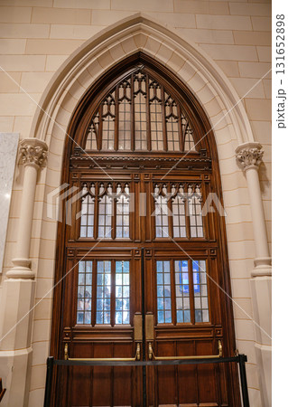 This photo features a grand wooden door with glass panels inside a cathedral. The pointed Gothic arch and stone columns add architectural elegance to the entryway. 131652898