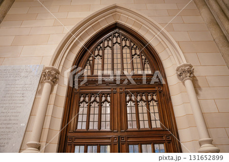 This photo captures a richly detailed wooden door set within a pointed Gothic arch in a stone cathedral interior. The door features intricate carved patterns and glass panels, framed by ornate columns This photo captures a richly detailed wooden door set within a pointed Gothic arch in a stone cathedral interior. The door features intricate carved patterns and glass panels, framed by ornate columns 131652899