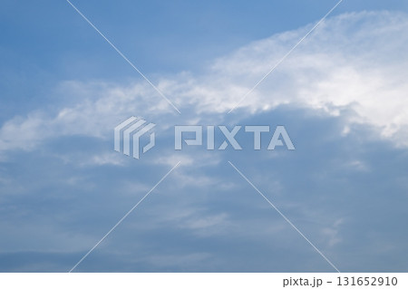 A view of a partly cloudy sky with sunbeams piercing through. Dark clouds sit at the bottom left, contrasting with the brighter, scattered clouds and the clear blue sky. 131652910
