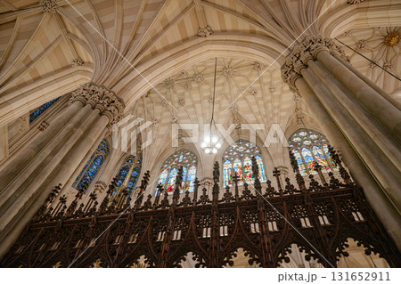 A view of the vaulted ceiling and vibrant stained glass windows inside a gothic-style cathedral. The intricate stone columns and ornate wooden railing enhance the beauty of this sacred space. 131652911