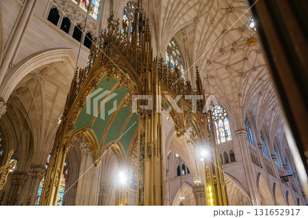 The image features a richly ornate golden canopy structure rising toward the intricately ribbed vaulted ceiling of a Gothic-style cathedral. Stained-glass windows and dramatic lighting highlight the 131652917