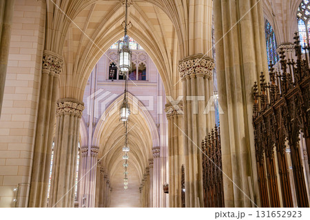 This image highlights a corridor of pointed arches, hanging lanterns, and stone columns inside St. Patrick's Cathedral in New York City. The Gothic Revival design is accentuated by soft light and This image highlights a corridor of pointed arches, hanging lanterns, and stone columns inside St. Patrick's Cathedral in New York City. The Gothic Revival design is accentuated by soft light and 131652923
