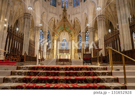The image captures the grand main altar of St. Patrick's Cathedral in New York City, framed by golden Gothic arches and stained glass windows. Ornate columns, carved woodwork, and rich red carpets The image captures the grand main altar of St. Patrick's Cathedral in New York City, framed by golden Gothic arches and stained glass windows. Ornate columns, carved woodwork, and rich red carpets 131652928