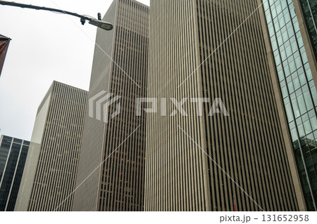 A group of tall skyscrapers with narrow vertical windows rises in Midtown Manhattan. The sharp vertical patterns create a powerful corporate atmosphere against the cloudy sky. A group of tall skyscrapers with narrow vertical windows rises in Midtown Manhattan. The sharp vertical patterns create a powerful corporate atmosphere against the cloudy sky. 131652958