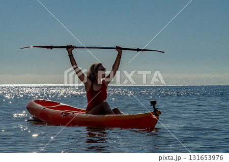 Kayaking, woman, ocean. Silhouetted woman in red swimsuit holding paddle above head on sparkling sea during summer vacation. Kayaking, woman, ocean. Silhouetted woman in red swimsuit holding paddle above head on sparkling sea during summer vacation. 131653976