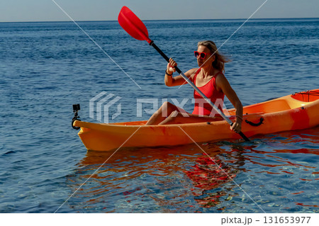 Kayaking, woman, ocean. A woman paddling an orange kayak on the clear blue ocean, enjoying an active summer vacation Kayaking, woman, ocean. A woman paddling an orange kayak on the clear blue ocean, enjoying an active summer vacation 131653977