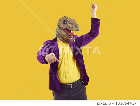 Man in purple suit and funny dinosaur mask dancing gangnam style on yellow background Man in purple suit and funny dinosaur mask dancing gangnam style on yellow background 131654417