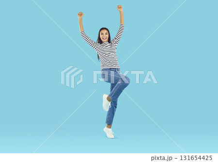 Optimistic woman standing on one leg with her hands raised Optimistic woman standing on one leg with her hands raised 131654425