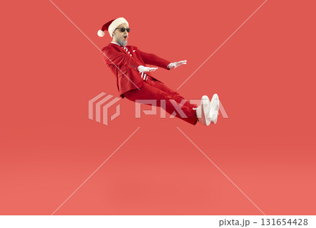Cheerful man with funny facial expression levitating in air isolated on red Christmas background. 131654428