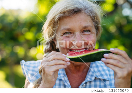 Lovely senior woman eating slice of watermelon in garden. 131655079