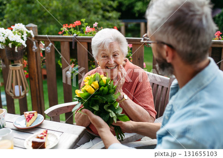 Mature bringing bringing flowers to his old mother. Mature bringing bringing flowers to his old mother. 131655103
