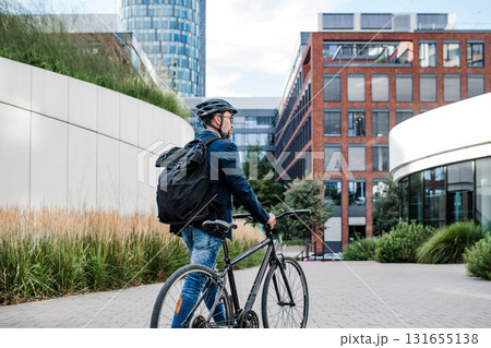City commuter walking with bike to office, wearing backpack and helmet. 131655138