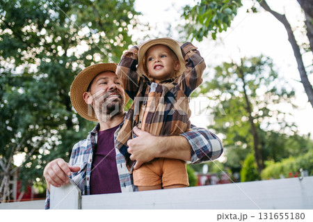 Little boy and father on farm, standing on fence. 131655180