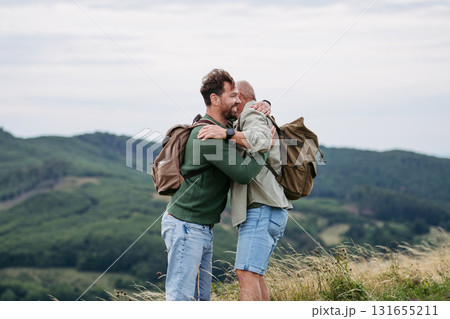 Adult son and older father hiking togeter in nature, hugging after finishing track. 131655211
