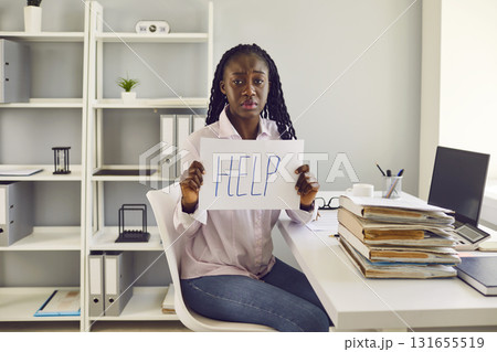 Tired woman sitting at desk at her workplace in office with pile of folders and a stack of papers. Tired woman sitting at desk at her workplace in office with pile of folders and a stack of papers. 131655519