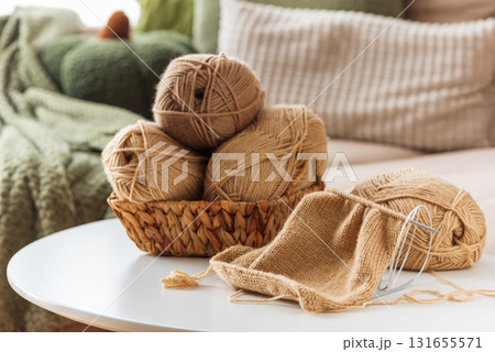 Knitting Basket with Yarn and Needles on White Table in Cozy Interior 131655571