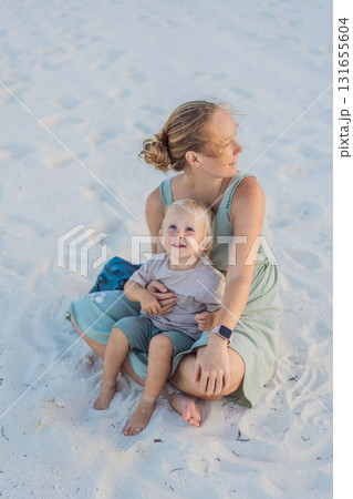 Mother and her little son sitting on a white sandy beach in Mexico during a peaceful evening, enjoying quality time together. Family bonding, summer relaxation, and vacation concept 131655604
