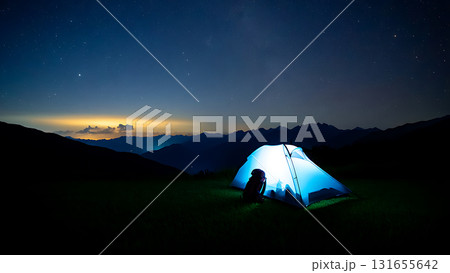 Illuminated tent glows beneath a starry sky with distant mountains and a backpack nearby at night 131655642
