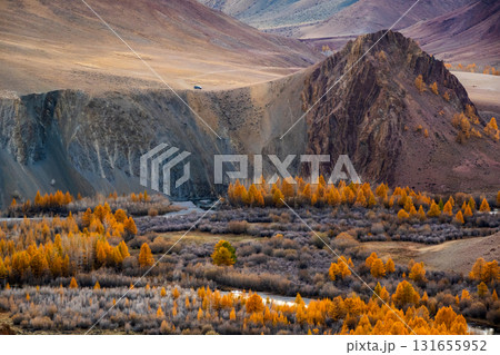 Autumn valley landscape with orange trees rugged mountains and a lone road vehicle in remote highlands 131655952