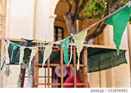 Close view of fabric bunting and pennant flags strung above market stall in urban courtyard, cheerful spring vibe Close view of fabric bunting and pennant flags strung above market stall in urban courtyard, cheerful spring vibe 131656061