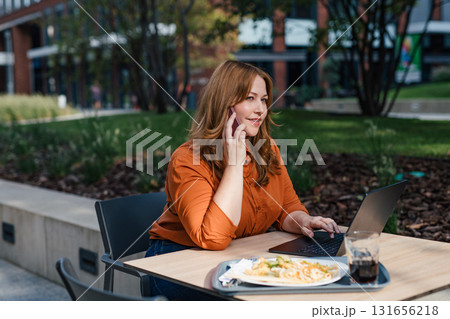 Plus size woman working remotely from restaurant, making phone call with client. 131656218