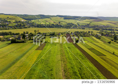 Aerial view of a small village win many houses and green agricultural fields in spring with fresh vegetation after seeding season on a warm sunny day. Aerial view of a small village win many houses and green agricultural fields in spring with fresh vegetation after seeding season on a warm sunny day. 131656966