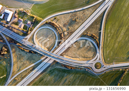 Aerial top view of modern highway road intersection, house roofs on spring green field background. Drone photography. Aerial top view of modern highway road intersection, house roofs on spring green field background. Drone photography. 131656990