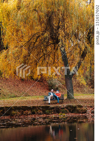 Son and older father sitting on bench by lake and talking. 131657602