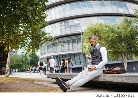 Handsome businessman in front of buildings in business district, looking at phone. 131657618