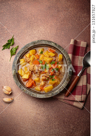 Chicken stew or soup with potatoes and carrots served in rustic bowl with spoon top view on dark brown concrete background 131657827