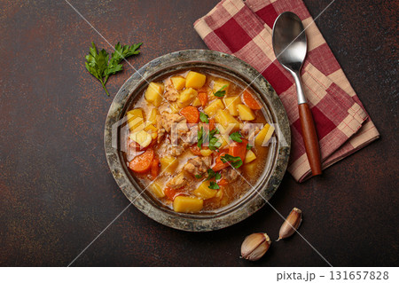 Chicken stew or soup with potatoes and carrots served in rustic bowl with spoon top view on dark brown concrete background Chicken stew or soup with potatoes and carrots served in rustic bowl with spoon top view on dark brown concrete background 131657828