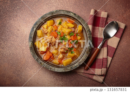 Chicken stew or soup with potatoes and carrots served in rustic bowl with spoon top view on dark brown concrete background 131657831