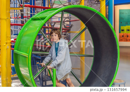 Teenage boy running inside a giant hamster-style wheel indoors, symbolizing energy, freedom, and playful childhood activity. Healthy lifestyle and youth concept 131657994