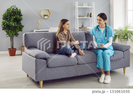 Child patient and woman pediatrician with clipboard sitting on couch and talking 131661030