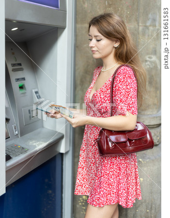 Woman uses ATM, withdraws cash from card. Girl buys travel ticket from machine Woman uses ATM, withdraws cash from card. Girl buys travel ticket from machine 131661583