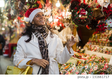 Hispanic woman in Santa hat choosing decorations at street Christmas fair 131661717