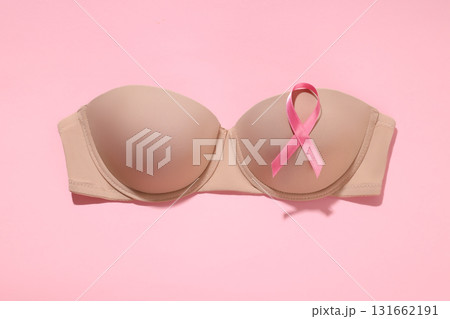Beige bra with a pink ribbon placed on a soft pink surface 131662191