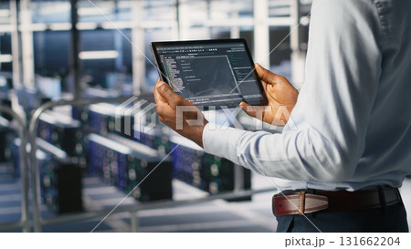 Data center admin checking code on tablet next to colleague reviewing AI visualizations in blurry background. IT experts use device to analyze neural networks outputs, ensuring stable gear operations 131662204